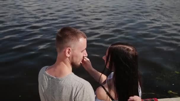 Un couple amoureux assis au bord de la rivière embrassant et embrassant . — Video