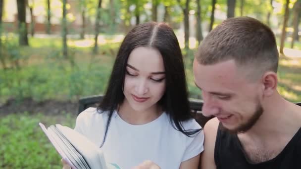 Dois amantes sentam-se em um banco e sorriem um para o outro assistindo fotos de família . — Vídeo de Stock