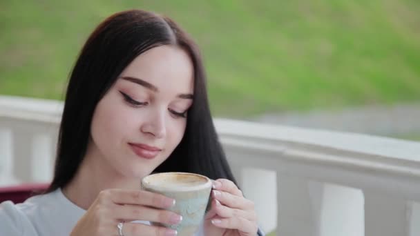 Ein sehr hübsches Mädchen trinkt Cappuccino auf der offenen Terrasse des Restaurants. — Stockvideo