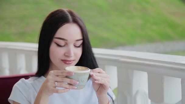 Uma menina muito bonita bebe cappuccino nos restaurantes terraço aberto . — Vídeo de Stock