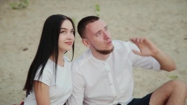 Sevgi dolu çift oturma plaj ve sarılma, günbatımı üzerinde.
