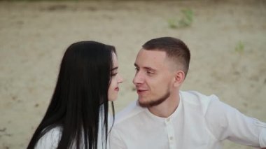 Sevgi dolu çift oturma plaj ve sarılma, günbatımı üzerinde.