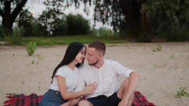 Sevgi dolu çift oturma plaj ve sarılma, günbatımı üzerinde.