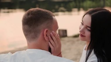 Sevgi dolu çift oturma plaj ve sarılma, günbatımı üzerinde.