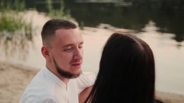 Sevgi dolu çift oturma plaj ve sarılma, günbatımı üzerinde.