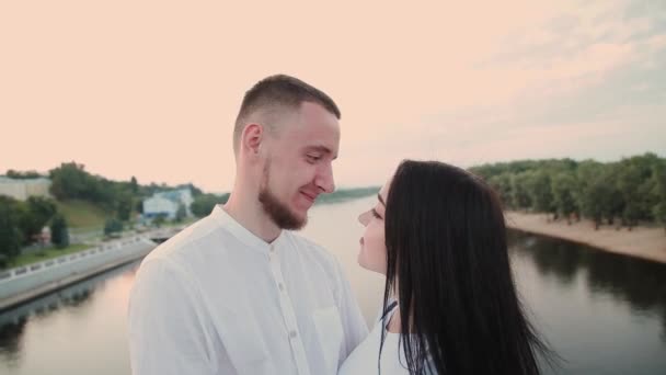 Ένα ζευγάρι ερωτευμένων στέκεται σε μια γέφυρα ενάντια σε ένα καταγάλανο ουρανό. — Αρχείο Βίντεο