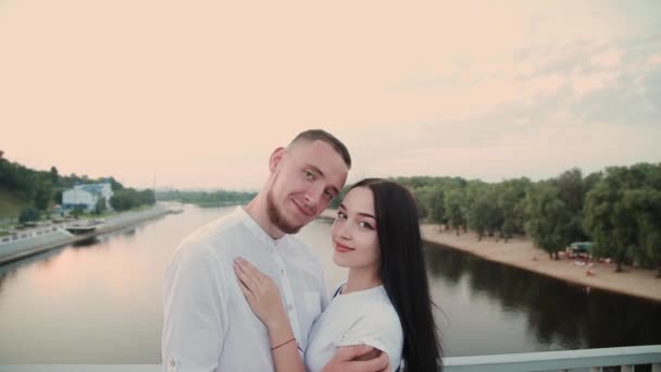 Una pareja amorosa está de pie en un puente contra un cielo azul . — Vídeo de stock