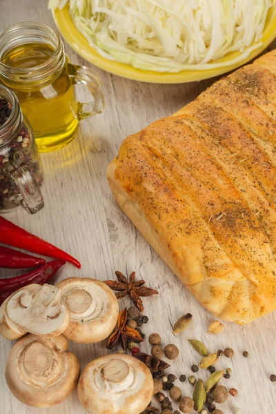 Pie with cabbage and mushrooms on a wooden background with ingredients. — Stock Photo, Image