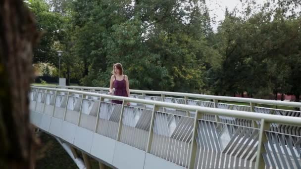 A very beautiful and sexy girl is standing on the bridge and looking to the distance. — Stock Video