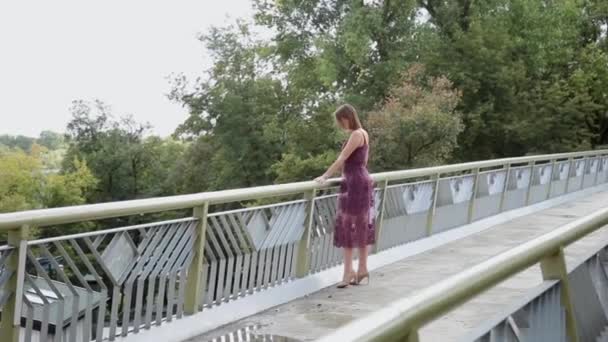 Uma menina muito bonita e sexy está de pé na ponte e olhando para a distância . — Vídeo de Stock