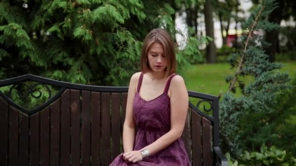 Πολύ όμορφη και σέξι κορίτσι που κάθεται σε ένα παγκάκι στο πάρκο. — Αρχείο Βίντεο