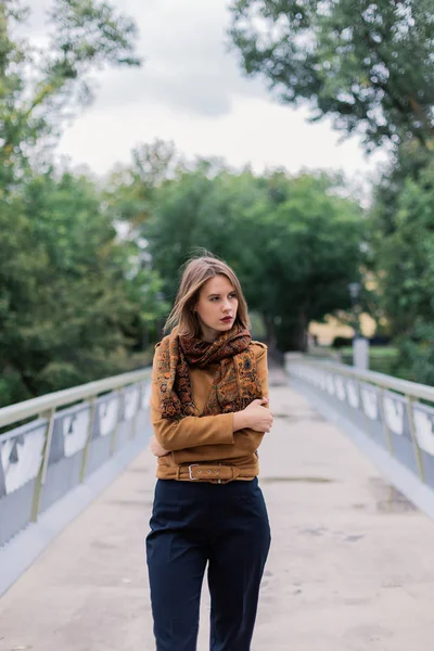 Uma menina muito bonita está de pé em uma ponte de ferro e está posando na câmera . — Fotografia de Stock