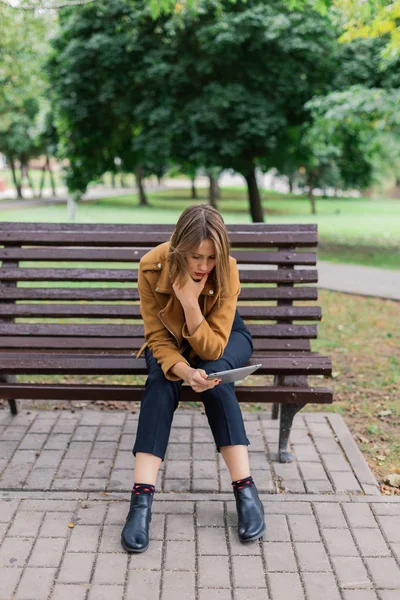 Schöne Mädchen sitzt auf einer Bank mit einem Tablet im Park. — Stockfoto