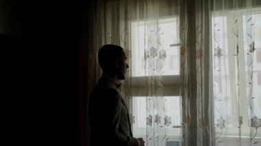 Genç işadamı koyar ve pencere tarafından ceket düzeltiyor.