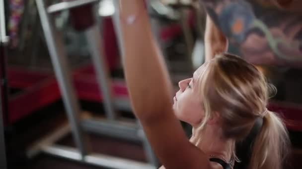 Een vrouw op de sportschool maakt oefeningen met behulp van een fitness-instructeur. — Stockvideo