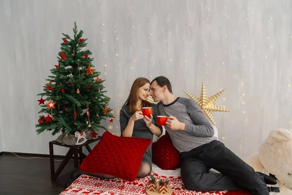 Couple familial sur le lit dans la chambre du Nouvel An tenant des tasses rouges avec thé . — Photo