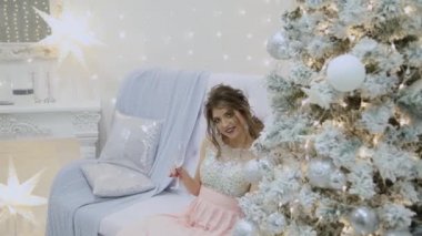 Çok güzel bir kız şampanya içiyor ve Yılbaşı dekor içinde kanepede oturuyor.