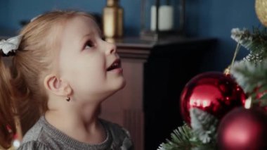 Çok güzel küçük kız yılbaşı ağacının yanında duruyor ve oyuncaklar dokunur.