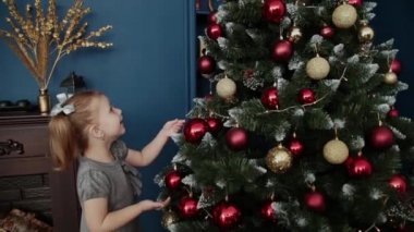 Çok güzel küçük kız yılbaşı ağacının yanında duruyor ve oyuncaklar dokunur.