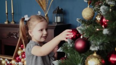 Çok güzel küçük kız yılbaşı ağacının yanında duruyor ve oyuncaklar dokunur