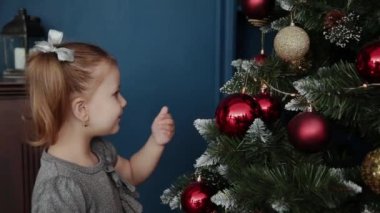 Çok güzel küçük kız yılbaşı ağacının yanında duruyor ve oyuncaklar dokunur.