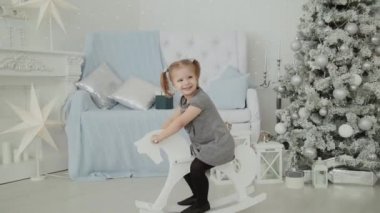 Yeni yıl odasında tahtadan bir at sürme ve gülümseyerek çok güzel küçük kız.