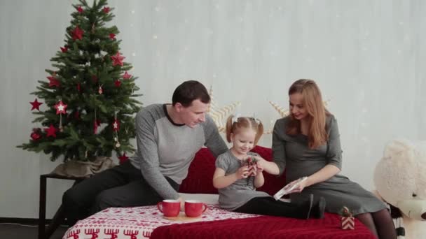 Manhã de Natal. A jovem família brinca alegremente uns com os outros. Em cima da cama um monte de almofadas, presentes de Natal em embalagens brilhantes e decorações de Natal. Feliz Natal 2019 . — Vídeo de Stock
