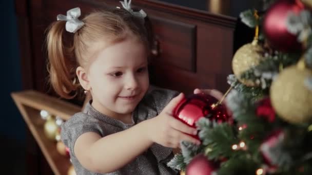 Zeer mooie meisje staat in de buurt van het nieuwe jaar boom en raakt speelgoed. — Stockvideo