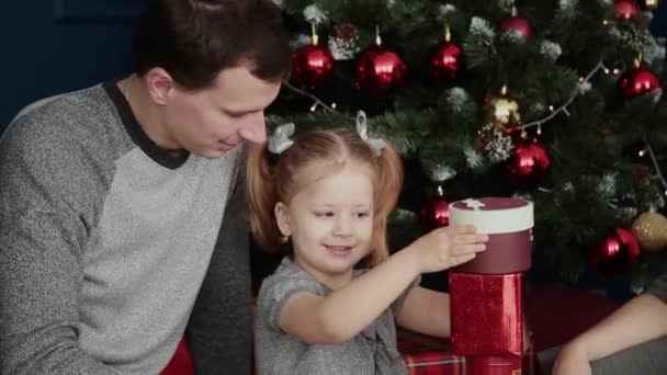 Una familia de tres abre regalos de Año Nuevo cerca de la chimenea, Navidad 2019 . — Vídeo de stock