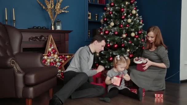 Une famille de trois ouvre cadeaux du Nouvel An près de la cheminée, Noël 2019 . — Video