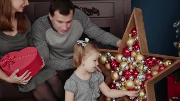 Una familia de tres abre regalos de Año Nuevo cerca de la chimenea, Navidad 2019 . — Vídeos de Stock