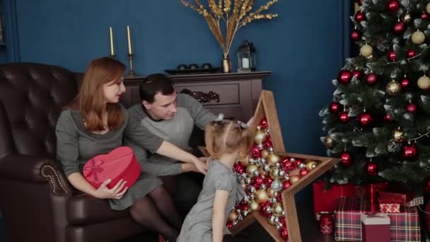 Een gezin van drie opent New Years geschenken in de buurt van de open haard, Kerstmis 2019. — Stockvideo