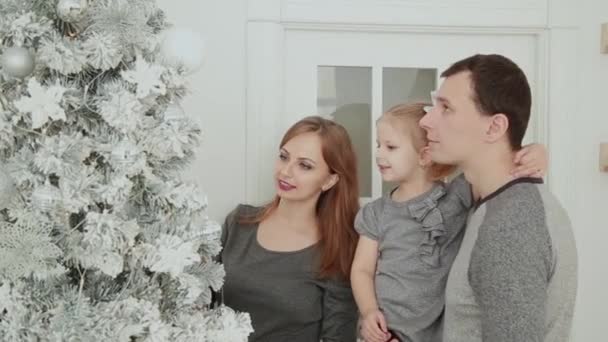 La familia está de pie cerca del árbol de Navidad, riendo hablando y tocando juguetes mientras espera la Navidad . — Vídeos de Stock