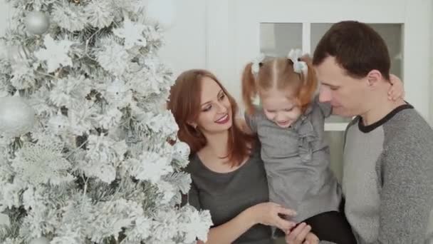 The family is standing near the Christmas tree, laughing talking and touching toys while waiting for Christmas. — Stock Video