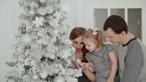 Rodzina jest stojący w pobliżu choinki, śmiejąc się mówi i dotykając zabawki podczas oczekiwania na Boże Narodzenie. — Wideo stockowe