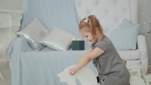 Very beautiful little girl riding on a wooden horse in the New Years room and smiling. — Stock Video