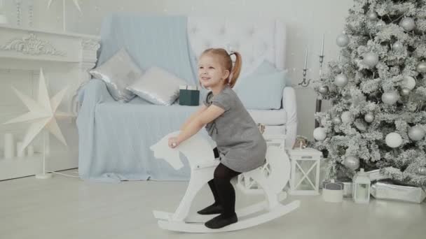 Muy hermosa niña montado en un caballo de madera en la habitación de Año Nuevo y sonriendo . — Vídeos de Stock