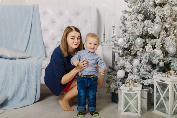 Porträt einer glücklichen Mutter und eines entzückenden Babys, die Weihnachten feiern. Neujahrsferien. Kleinkind mit Mama im festlich geschmückten Raum mit Christbaum und Dekoration. — Stockfoto