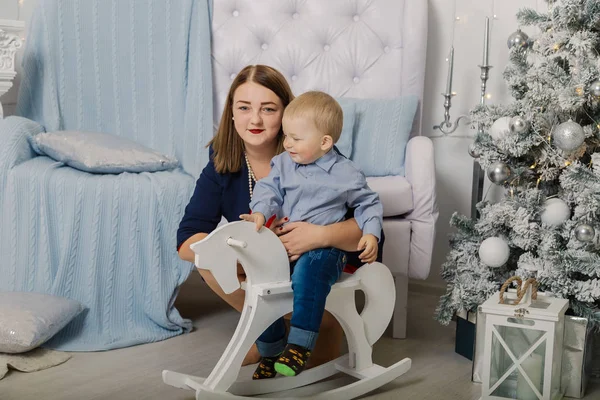 Porträt einer glücklichen Mutter und eines entzückenden Babys, die Weihnachten feiern. Neujahrsferien. Kleinkind mit Mama im festlich geschmückten Raum mit Christbaum und Dekoration. — Stockfoto