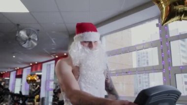 Spor salonunda fitness eğitmeni Noel Baba koşu bandı üzerinde çalışan.