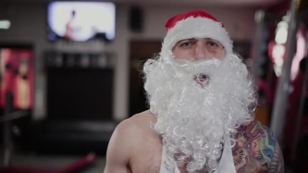 Santa Claus v tělocvičně se šklebící a ukazuje biceps. — Stock video