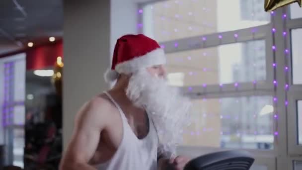 Bir koşu bandı ve palyaçoluk spor salonunda fitness eğitmeni Noel Baba çalışır. — Stok video