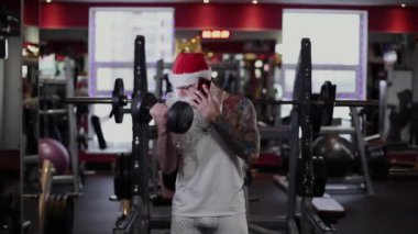 Spor salonunda bir halter kaldırma ve telefonda konuşurken fitness eğitmeni Noel Baba.