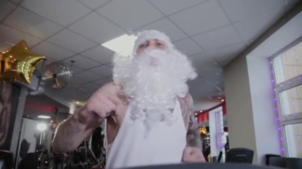 Instruktor fitness Santa Claus w siłowni działa na bieżni i grymasy. — Wideo stockowe