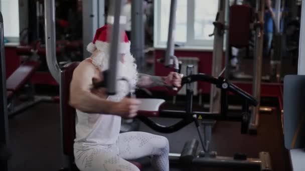 Fitnesstrainer Weihnachtsmann im Fitnessstudio am Simulator. — Stockvideo