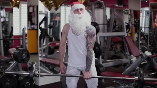 Fitness instruktor Santa Claus v tělocvičně vyvolává činka a grimasy. — Stock video