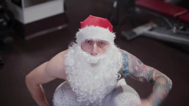 Fitness instructeur Santa Claus in de sportschool verhoogt de barbell en grimaces. — Stockvideo