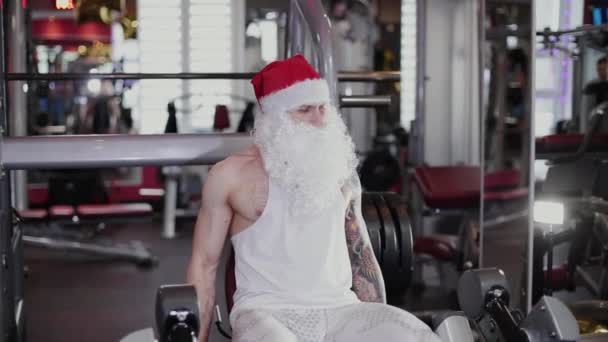 Instruktor fitness Santa Claus w siłowni trenuje nogi na symulatorze. — Wideo stockowe