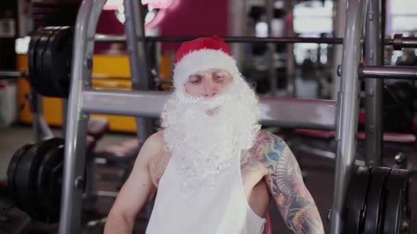 Instructor de fitness Santa Claus en el gimnasio entrena sus piernas en el simulador . — Vídeos de Stock