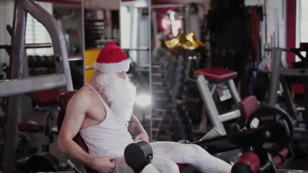 Bacaklarını simülatör spor salonunda fitness eğitmeni Noel Baba eğitiyor. — Stok video